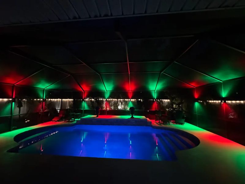 Pool cage at night lit with vibrant red and green RGB scene over blue pool