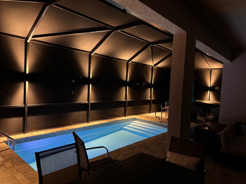 Pool cage with warm white LED sconces casting symmetrical glow patterns at night in Wesley Chapel