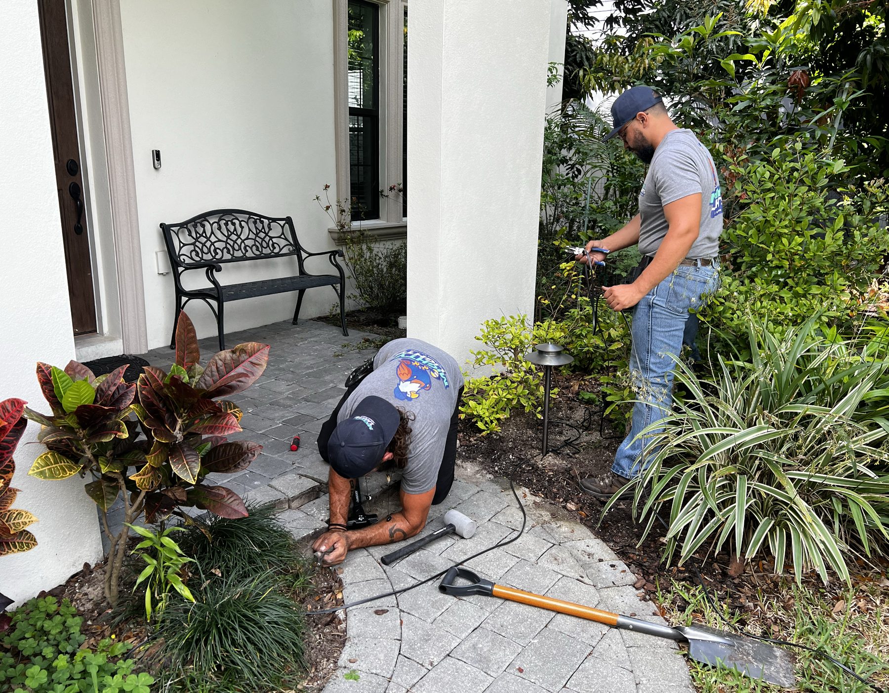 Mighty Lights crew on-site repairing landscape lighting fixtures at a Tampa Bay home, tools and shovel on the walkway
